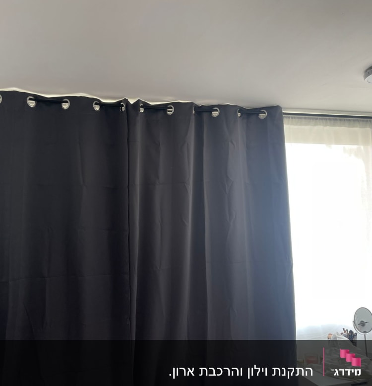 וילון כהה תלוי על מוט ליד חלון מואר